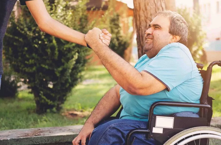 Henkilökohtainen avustaja puristaa pyörätuolisssa istuvan avustettavan kättä Espoossa
